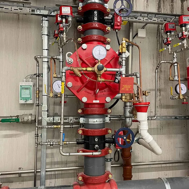 Nærbilde av ventil og manometre i et sprinkleranlegg montert på vegg.